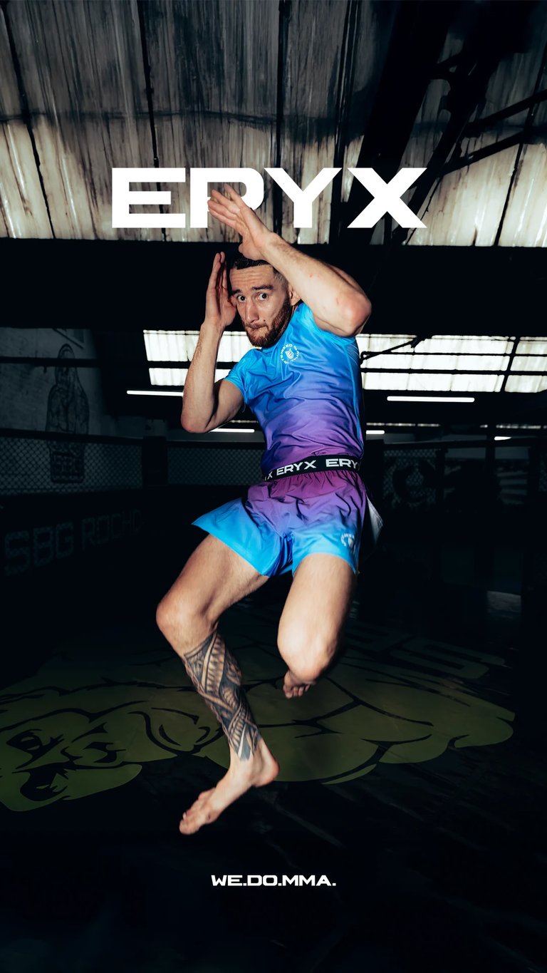 Male athlete in blue and purple ERYX sportswear performing a dynamic jumping kick in an indoor gym facility