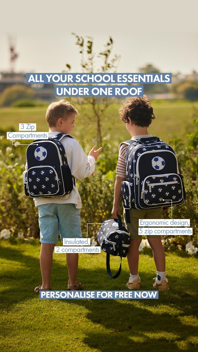 Two children wearing school backpacks with soccer ball design standing outdoors in a green field, showing back-to-school essentials