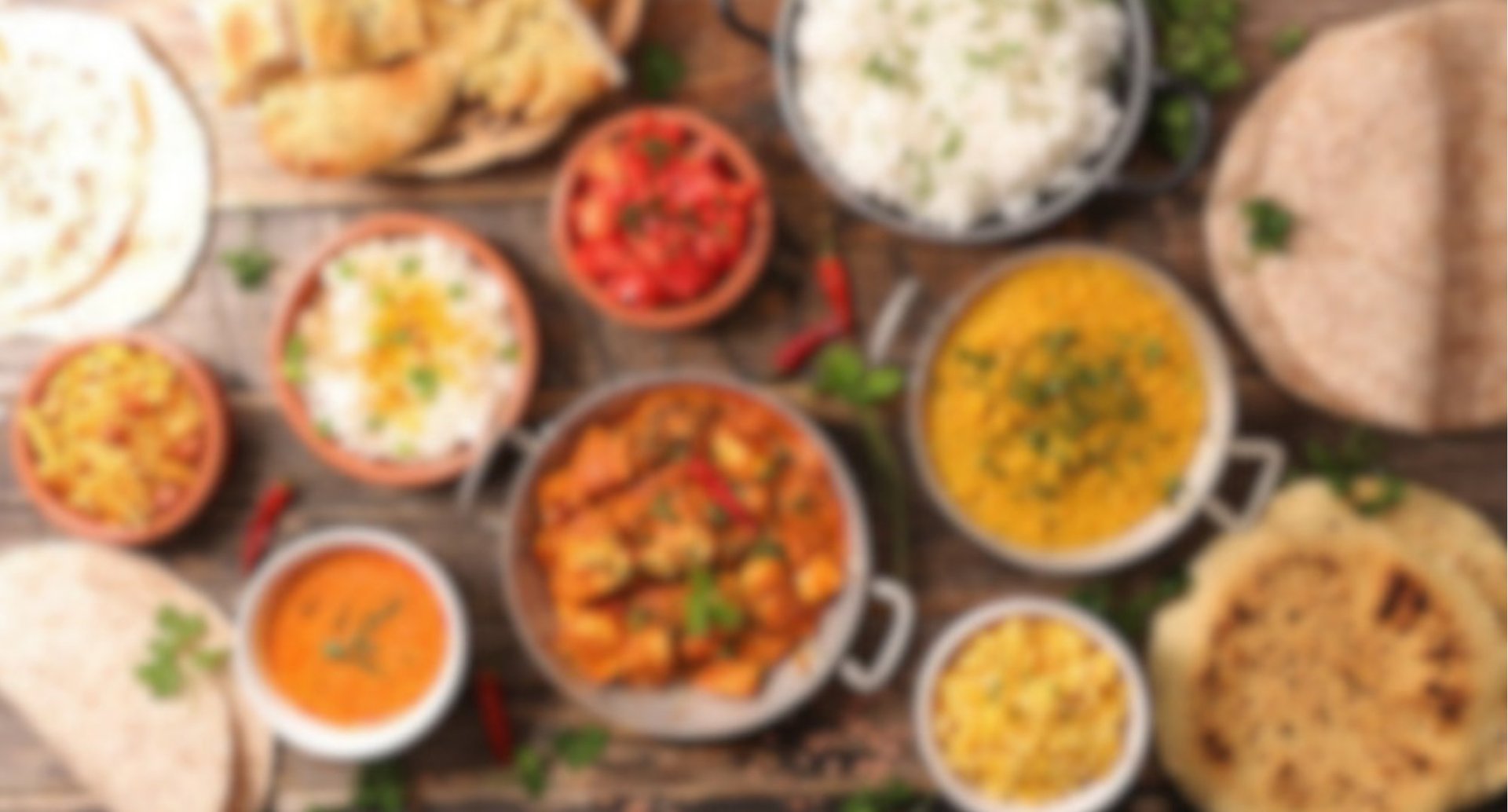 Overhead view of Indian cuisine spread with curries, dals, rice, naan bread and various condiments in bowls