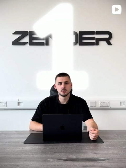 Man in black shirt sitting at desk with laptop in front of ZER1DER branding sign
