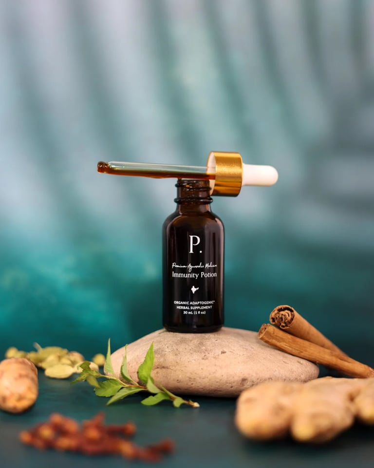 Black dropper bottle labeled P with gold pipette on smooth stone surrounded by natural ingredients including cinnamon sticks and botanicals