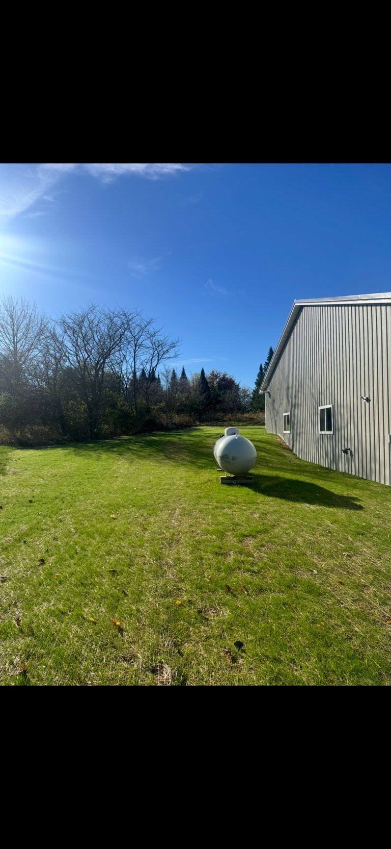 Large white spherical tank on green lawn beside corrugated metal shed under clear blue sky with trees in background