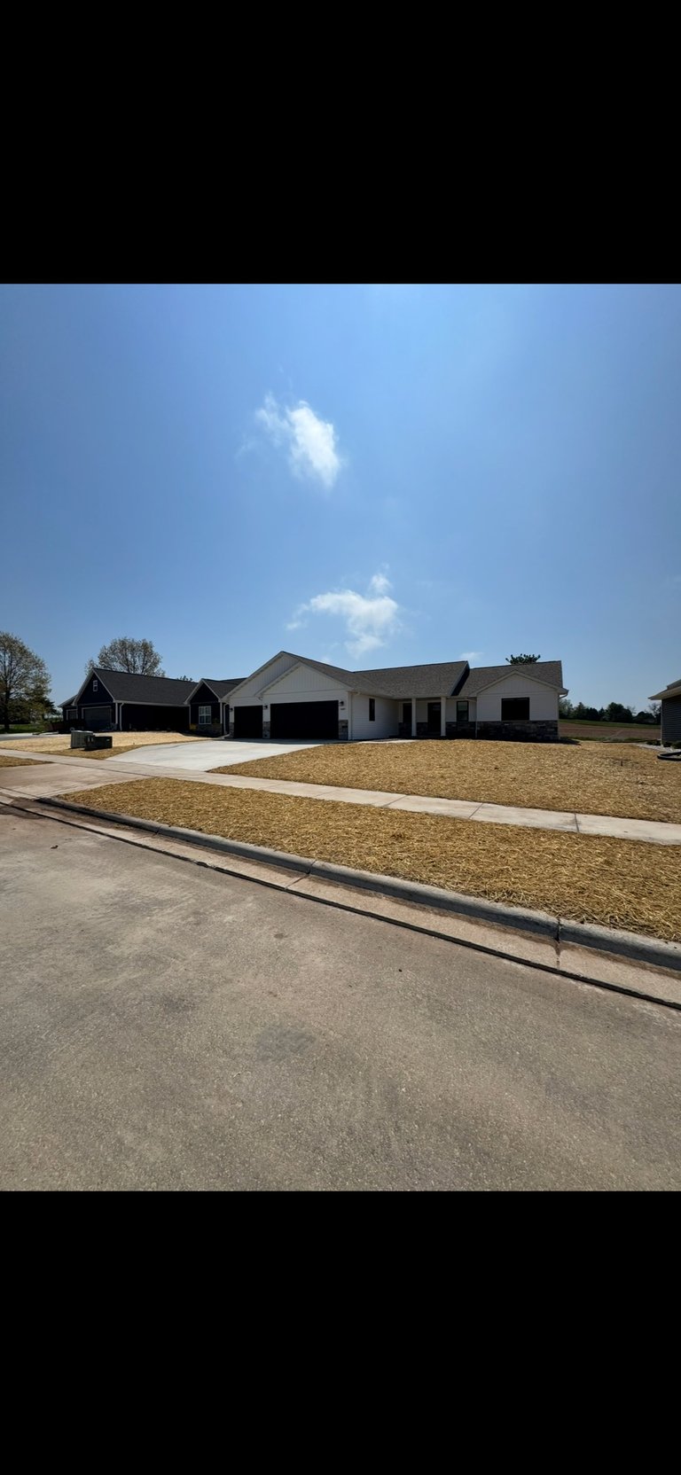 New two-car garage residential home on flat lot with driveway under clear blue sky