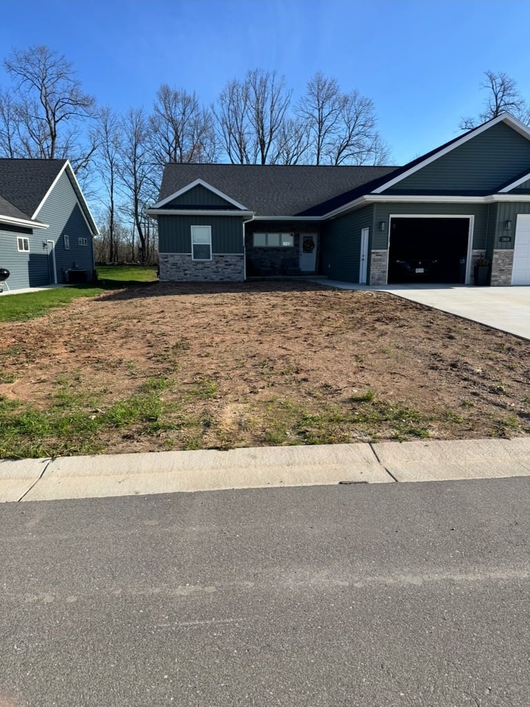 New single-story dark blue house with attached garage on bare dirt lot, bare trees visible, clear sky