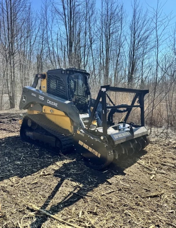 John Deere compact track loader with brush cutter attachment in a winter forest clearing