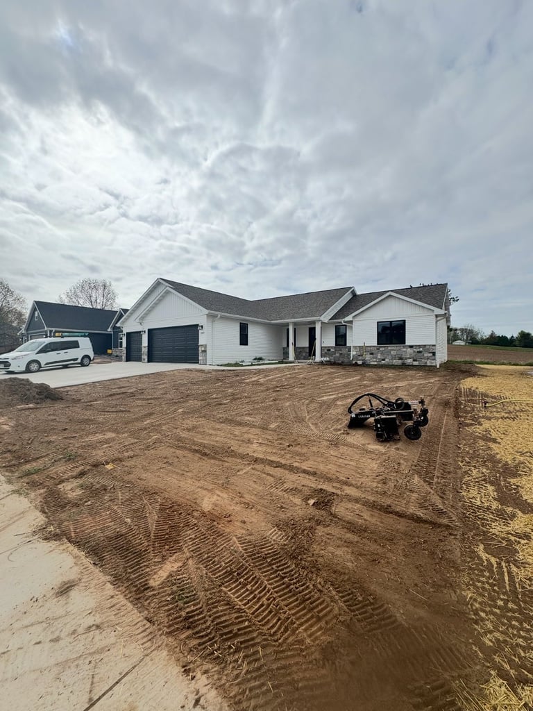 New white house under construction with graded dirt yard, parked vehicle, and cloudy sky