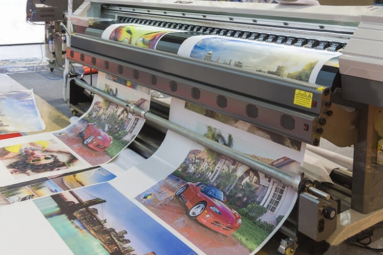 Large format inkjet printer outputting colorful photographic prints onto glossy paper in a print production facility