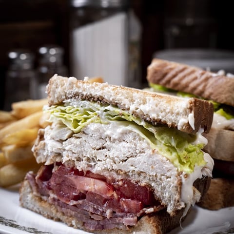 Stacked deli sandwich with roast beef, turkey, lettuce and mayonnaise on toasted bread, served on white plate