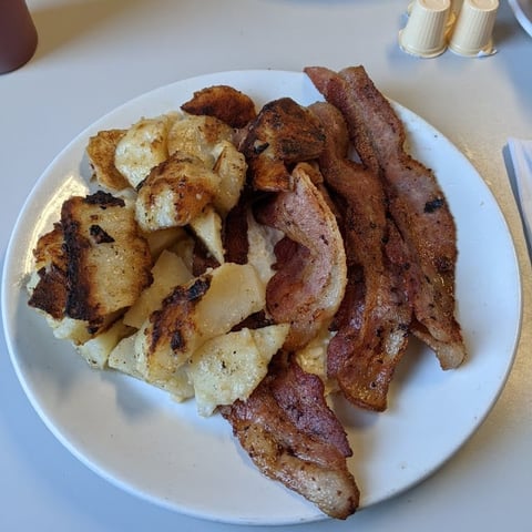 A white plate with crispy bacon strips and golden hash browns served at a restaurant table