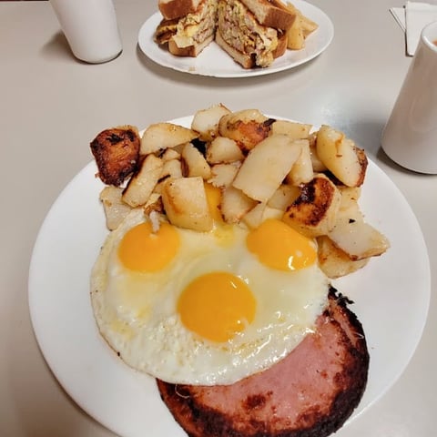 Breakfast plate with two sunny-side-up eggs, crispy ham, and roasted potatoes, with toast and milk on the table