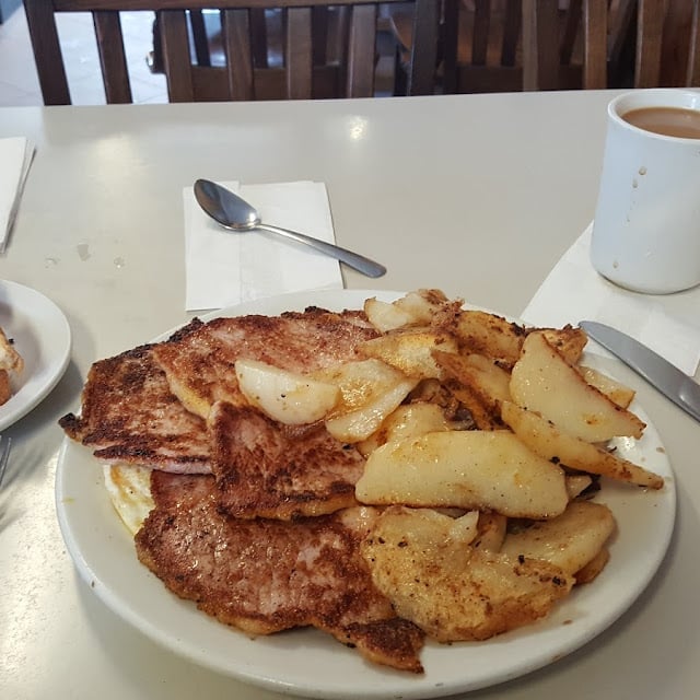 A plate of crispy hash browns and golden-brown pancakes served in a diner, with a white mug of coffee in the background