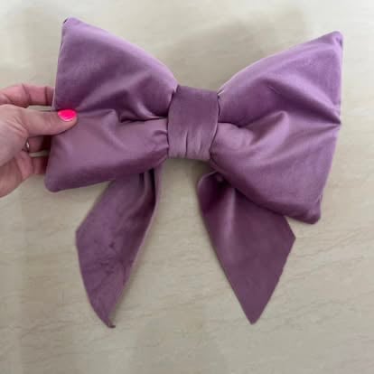 Hand holding a large purple fabric bow with four pointed loops against a beige background
