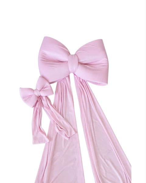 Pink satin bow with flowing ribbons and smaller decorative bow accent against white background