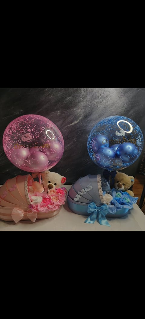 Two decorative gift baskets with glowing planet orbs on top - one pink and one blue - each containing teddy bears and flowers with ribbons.