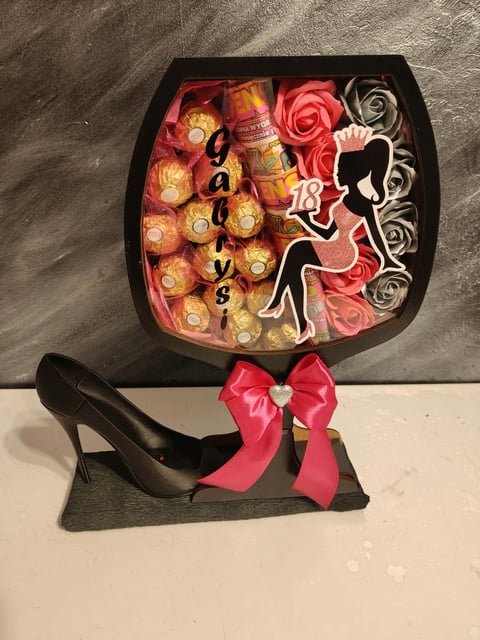 Decorative gift box shaped like a high heel shoe with chocolates, rose flowers, and pink bow on display stand