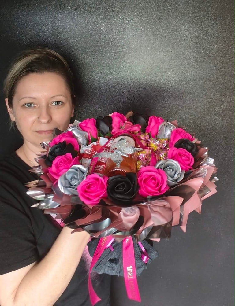 Kobieta trzymająca elegancki bukiet z różowych, srebrnych i czarnych sztucznych róż, czekoladkami i różowymi wstążkami Just For You na szarym tle