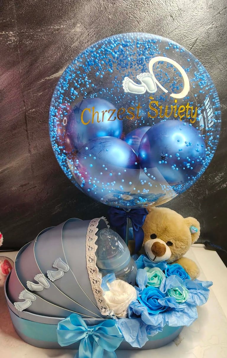 Niebieski prezent Chrzest Święty z dużym przezroczystym balonem-bąbelkiem wypełnionym niebieskimi balonami i niebieskim pyłem, pluszowym brązowym misiem, butelką z niebieską nakrętką oraz niebieskimi i błękitnymi piankowymi różami