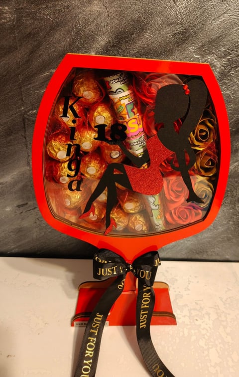 Red heart-shaped gift box containing chocolates, a candle, and decorative items with a black ribbon bow