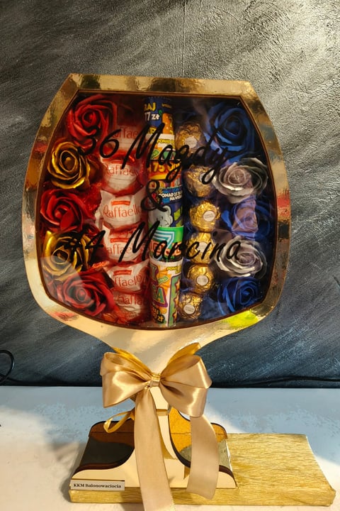 Luxury gift arrangement with red, gold, and blue roses, chocolates, and candies in a gold-trimmed box with a cream ribbon bow