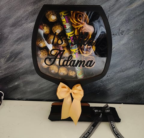 Black Adama branded chocolate bouquet with golden candies, yellow ribbons, and decorative elements in a fan-shaped box arrangement