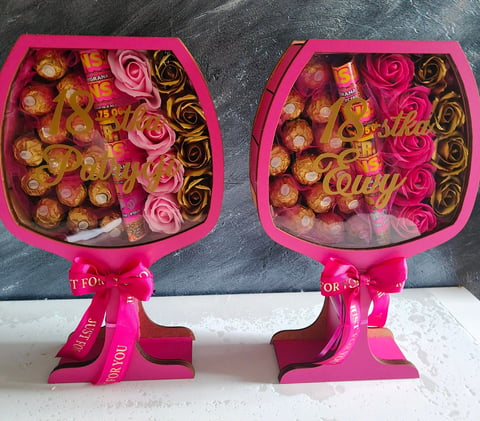 Two pink decorative boxes filled with assorted chocolates, golden truffles, and pink roses with golden scrolls and pink ribbons