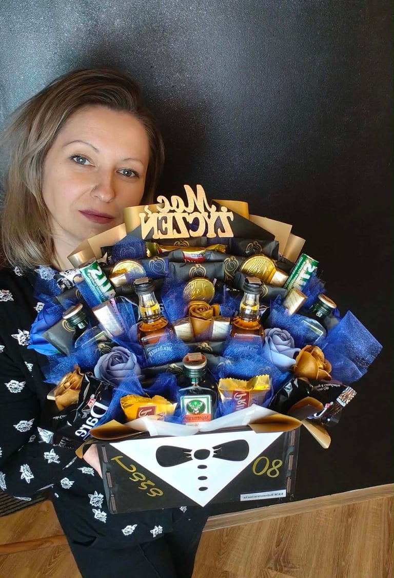 Kobieta trzymająca duży bukiet prezentowy z produktami kosmetycznymi i perfumami, w niebieskim papierze ze złotą wstęgą