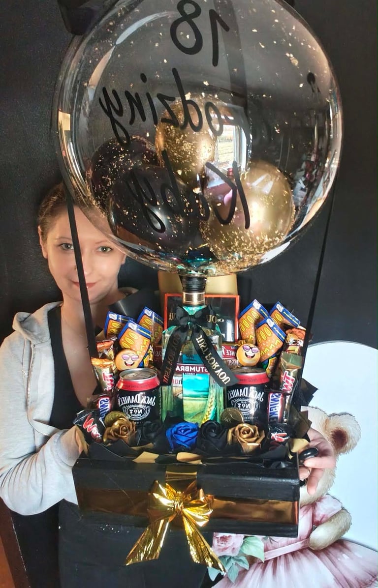 Kobieta trzymająca ogromną loterię-balon z Jack Daniel's w środku, otoczoną chipsami Lay's, M&M's, drinkiem Dr Witt i złotymi czekoladkami, z czarno-złotą wstążką