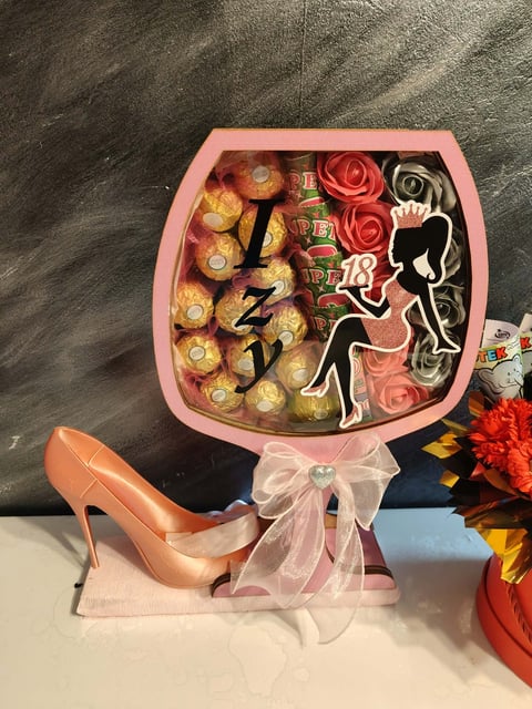 Pink bouquet-shaped gift box filled with chocolates, silk roses, and decorative elements, tied with a white ribbon bow