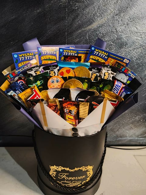 A luxury gift box filled with assorted snacks, lottery tickets, and candy arranged in a black and gold branded container with white wrapping paper.