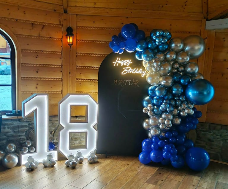 18th birthday party display with large white numbers, blue and silver balloon arch, and black Happy Birthday Arthur sign in wooden venue