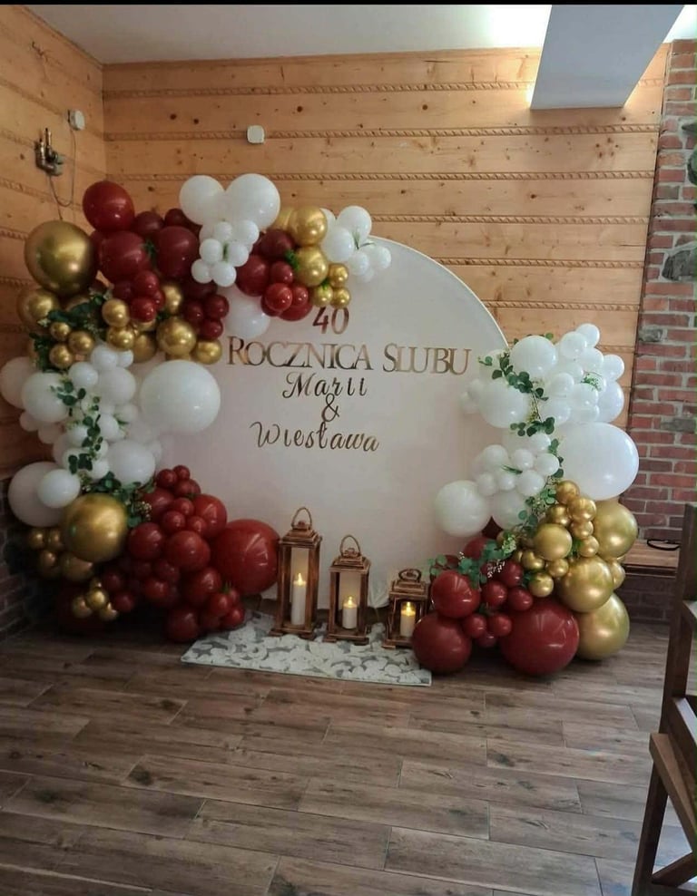 Elegant wedding backdrop with ROCZNA SUBU Mari Mieslawa text, decorated with red, white, and gold balloons, greenery, and lanterns