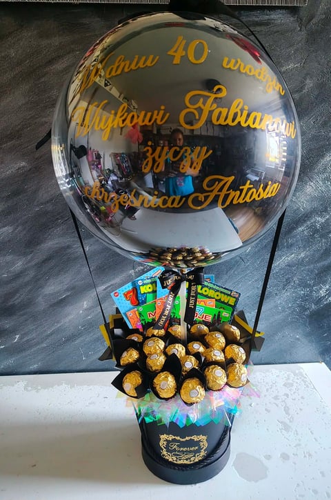 Decorative hot air balloon centerpiece made with golden chocolate balls and candy, topped with personalized clear bubble and black ribbon bow