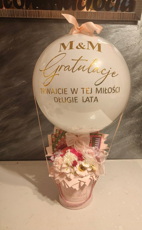 M&M congratulations hot air balloon decoration with pink flowers and peach ribbon in a basket