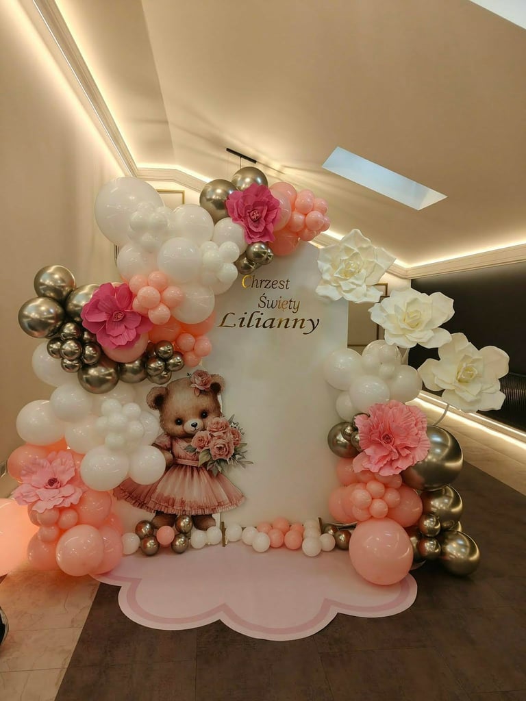 Ścianka Chrzest Święty Lilianny z różowo-białym łukiem balonowym, brązowym misiem w różowej sukience, złotymi kulami, ogromnymi białymi różami i napisem Chrzest Święty Lilianny