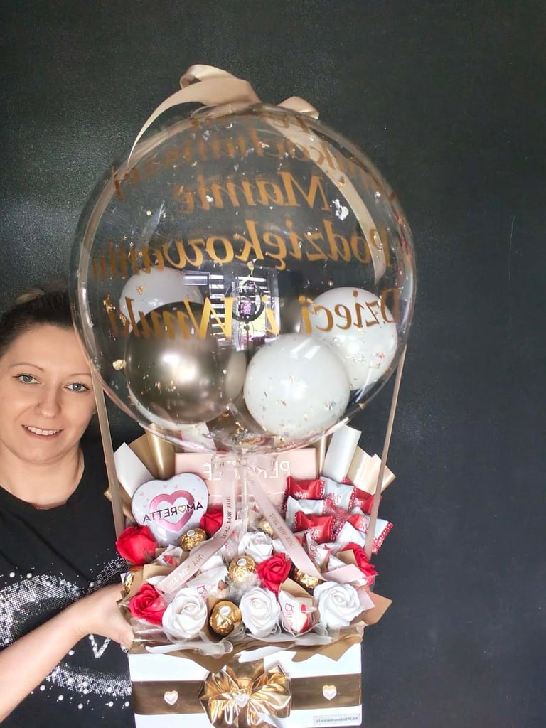 Kobieta stojąca obok wielkiej dekoracji balonowej w kształcie balonu na ogrzaną, z kwiatami i złotymi prezentami przymocowanymi do koszyka, z różowymi wstążkami
