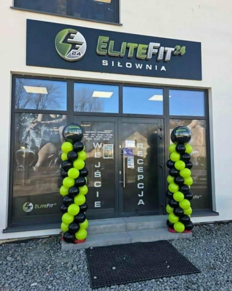 Otwarcie siłowni EliteFit24 z dwiema czarno-neonowo-zielonymi kolumnami balonowymi przy drzwiach wejściowych