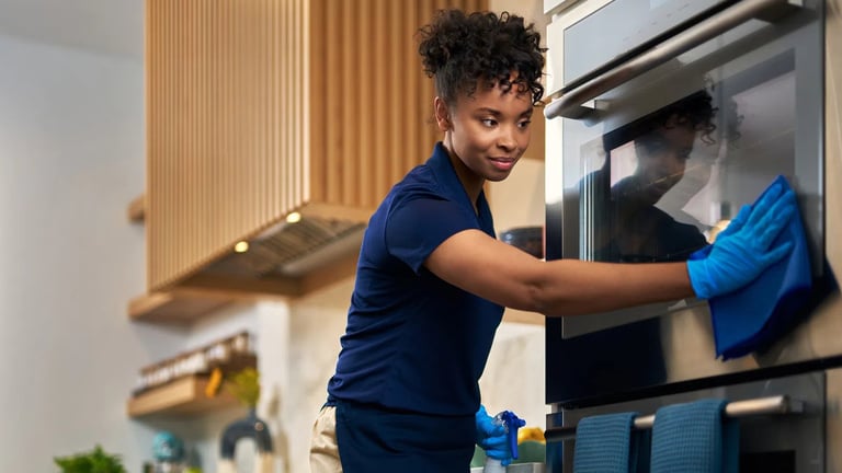 Woman in navy shirt cleaning microwave oven with blue cloth in modern kitchen