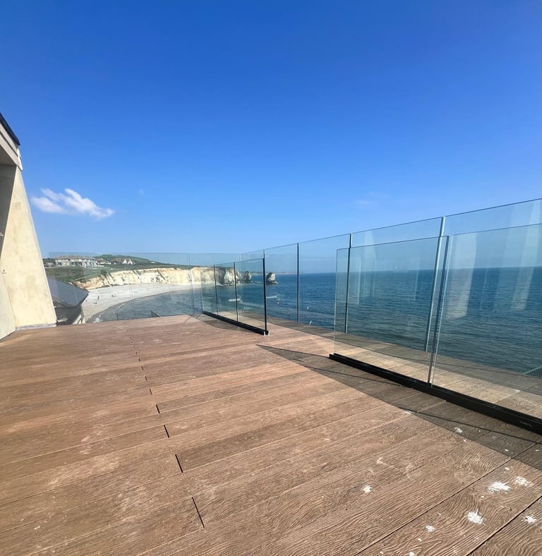 Wooden deck with glass railing overlooking coastal cliffs and blue ocean under clear sky