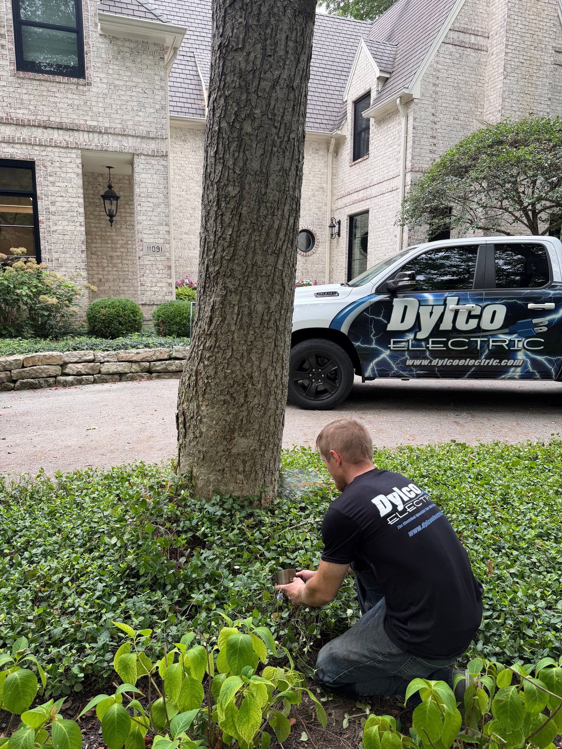 Dylco Electric technician inspecting landscaping and trees in the front yard of a brick Westfield home