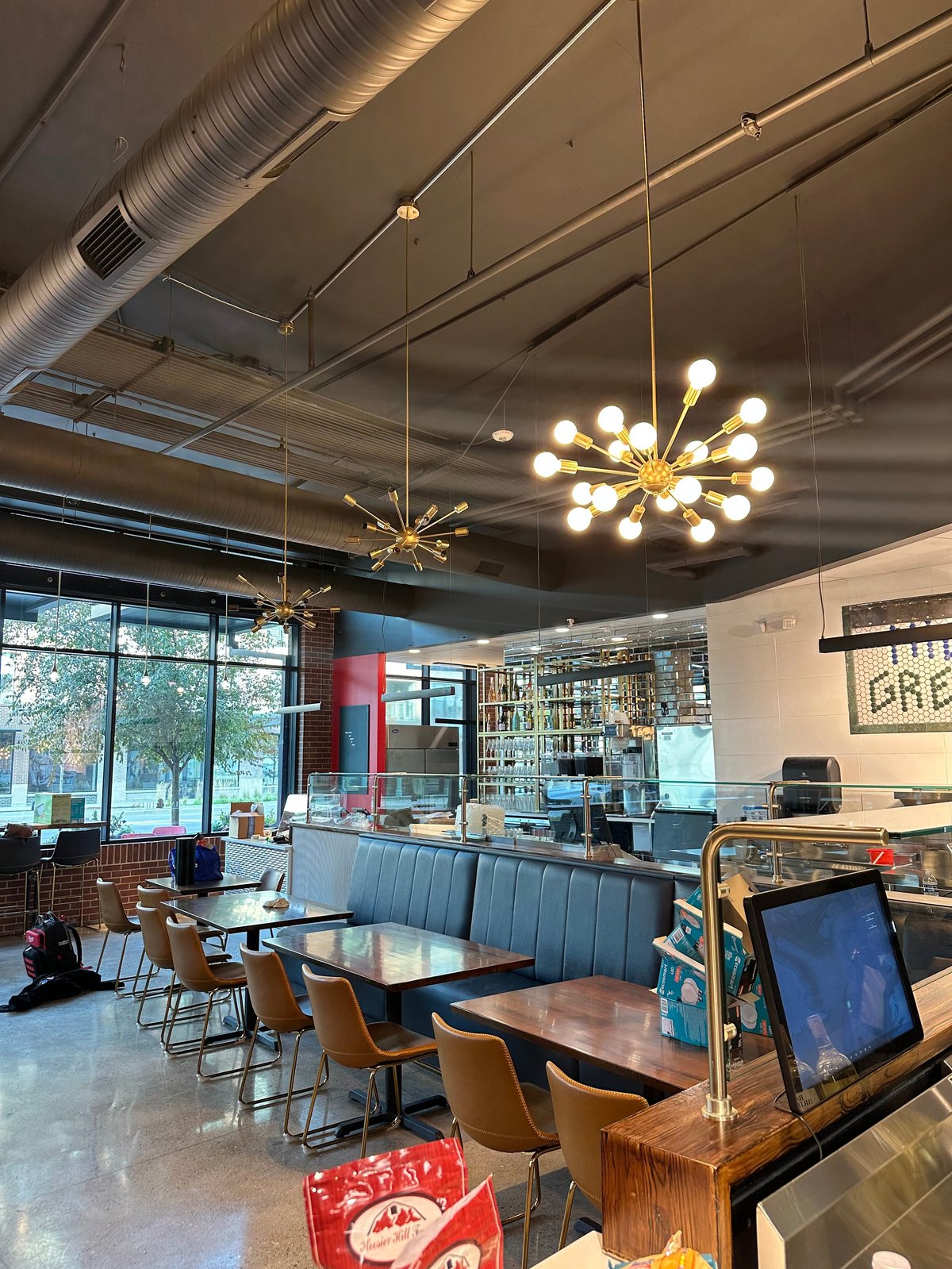 Modern café interior with pendant lights, dining tables, blue booth seating, counter service area, and large windows overlooking outdoor space