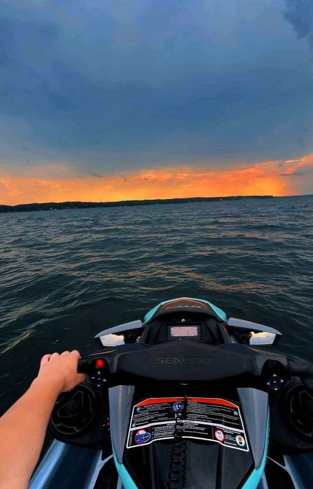 Person riding a jet ski on the ocean during sunset with orange and blue sky reflected on the water