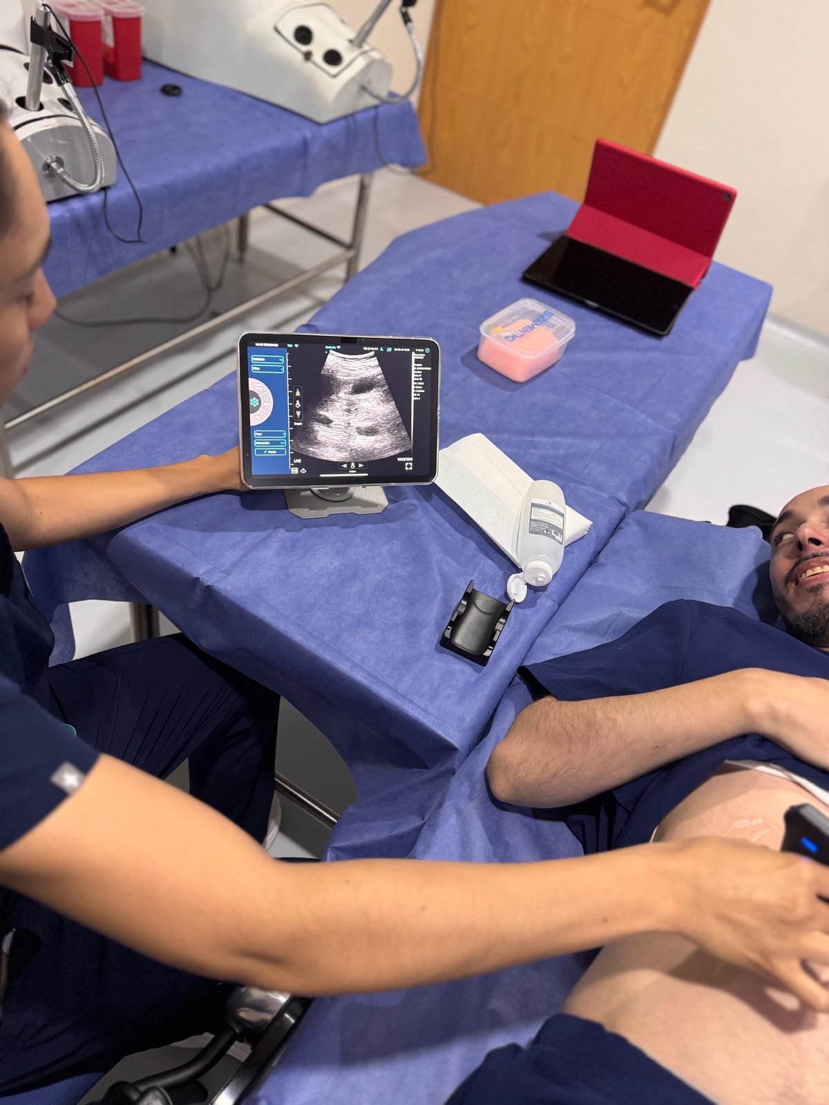 Sonógrafo realizando ultrasonido abdominal con dispositivo MY11 sobre mesa azul