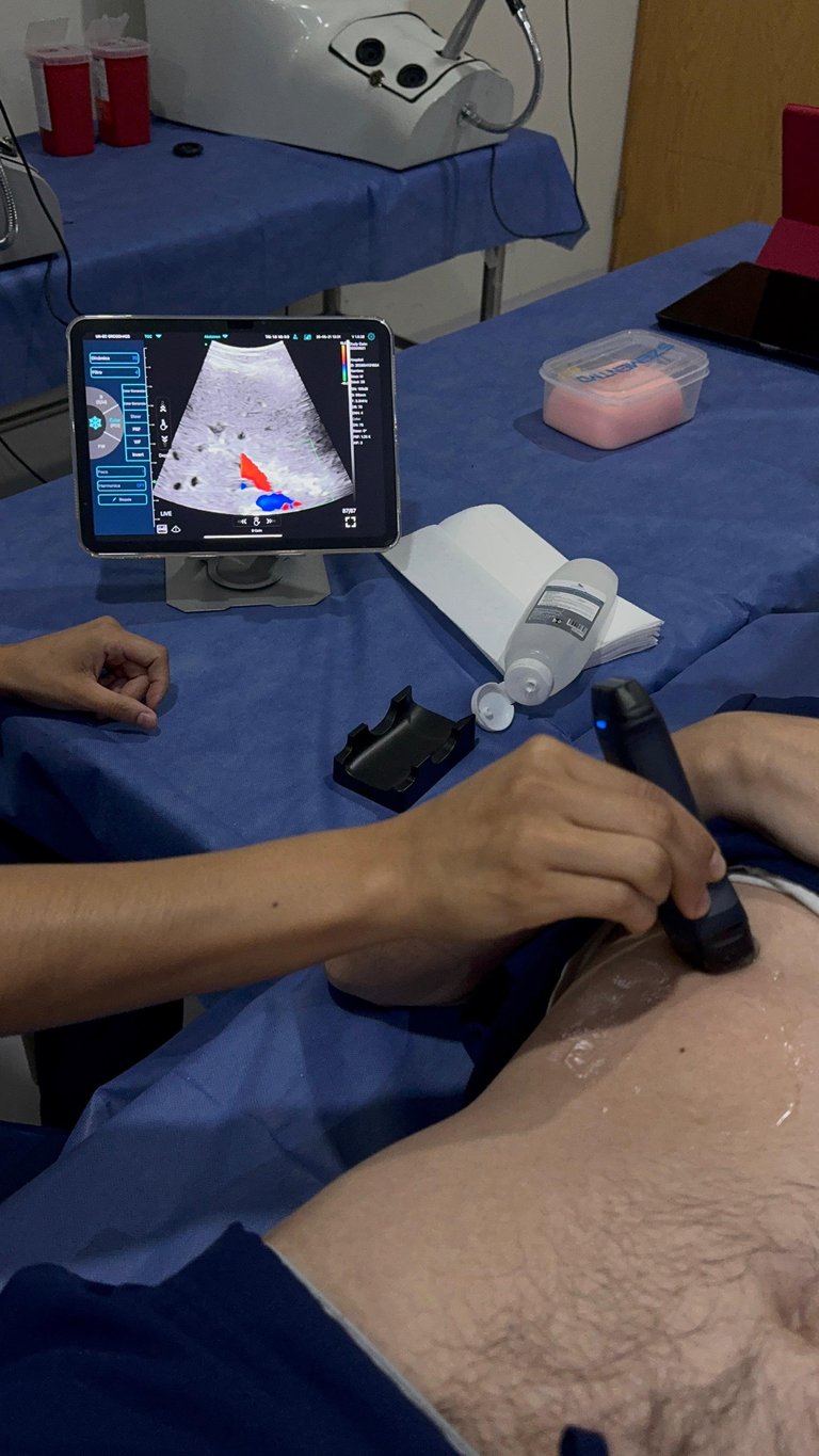 Examen de ultrasonido en brazo del paciente con sonda de mano y tablet mostrando imagen
