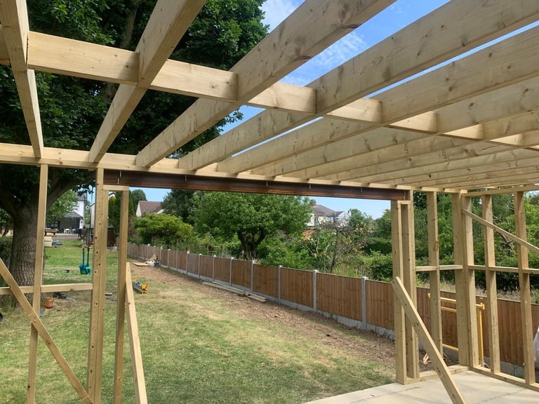 Wooden pergola frame under construction in backyard with wooden fence and green landscaping