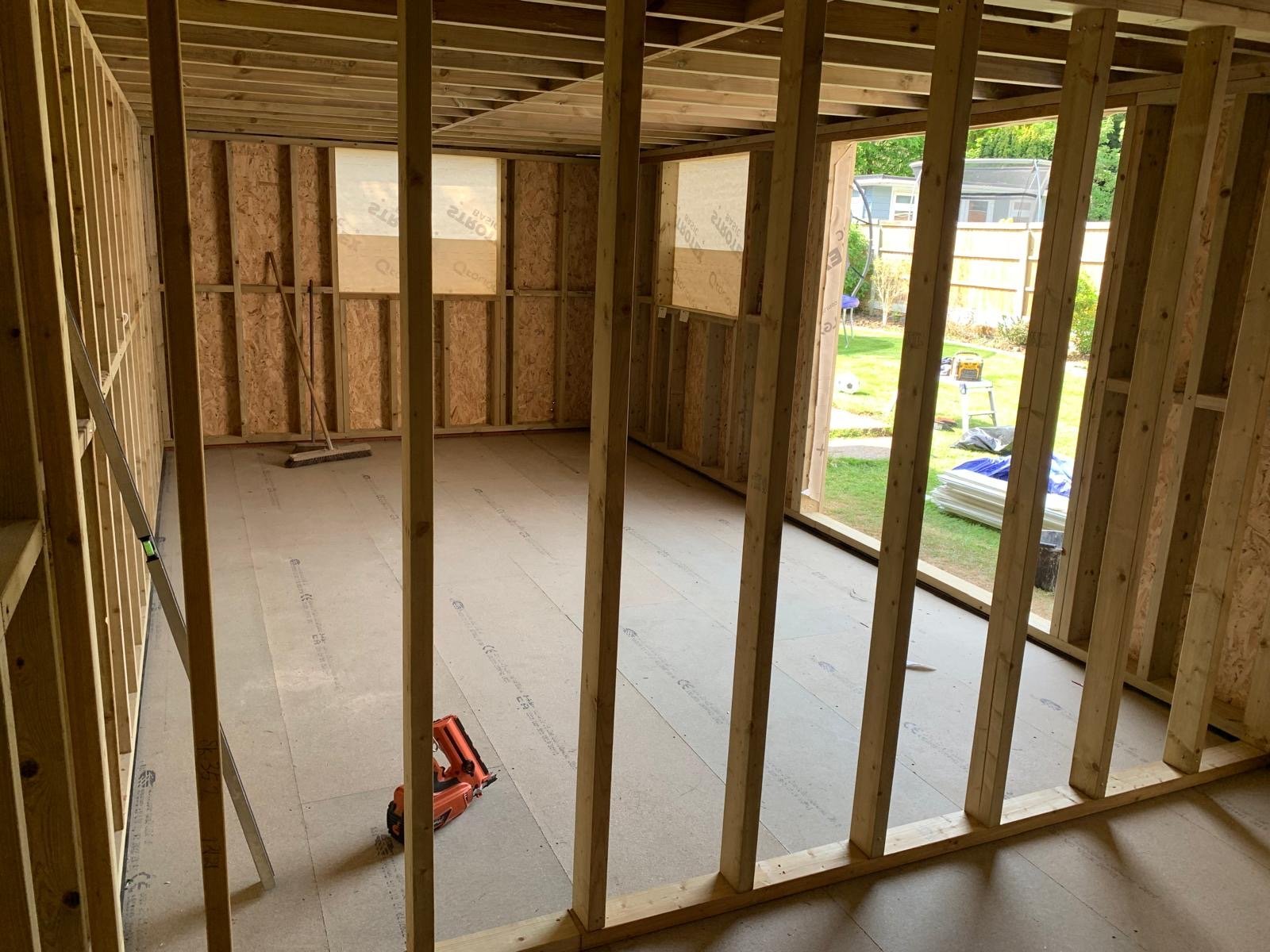 Interior of wooden framed room under construction with concrete floor and large windows showing outdoor yard