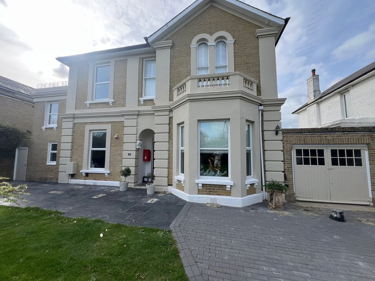 Two-story stone townhouse with attached garage, manicured lawn, and paved driveway on a sunny day.