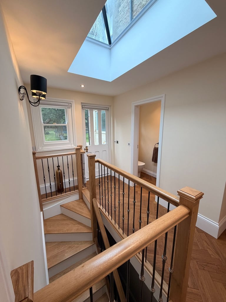 Modern staircase landing with wooden railings, skylights, and views of interior doors and windows
