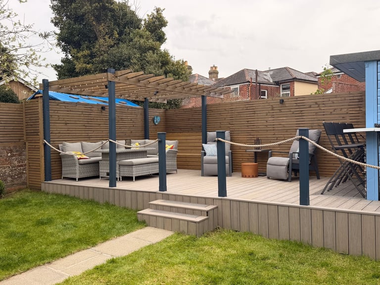 Modern backyard patio with wooden deck, pergola, outdoor furniture, and metal posts overlooking lawn
