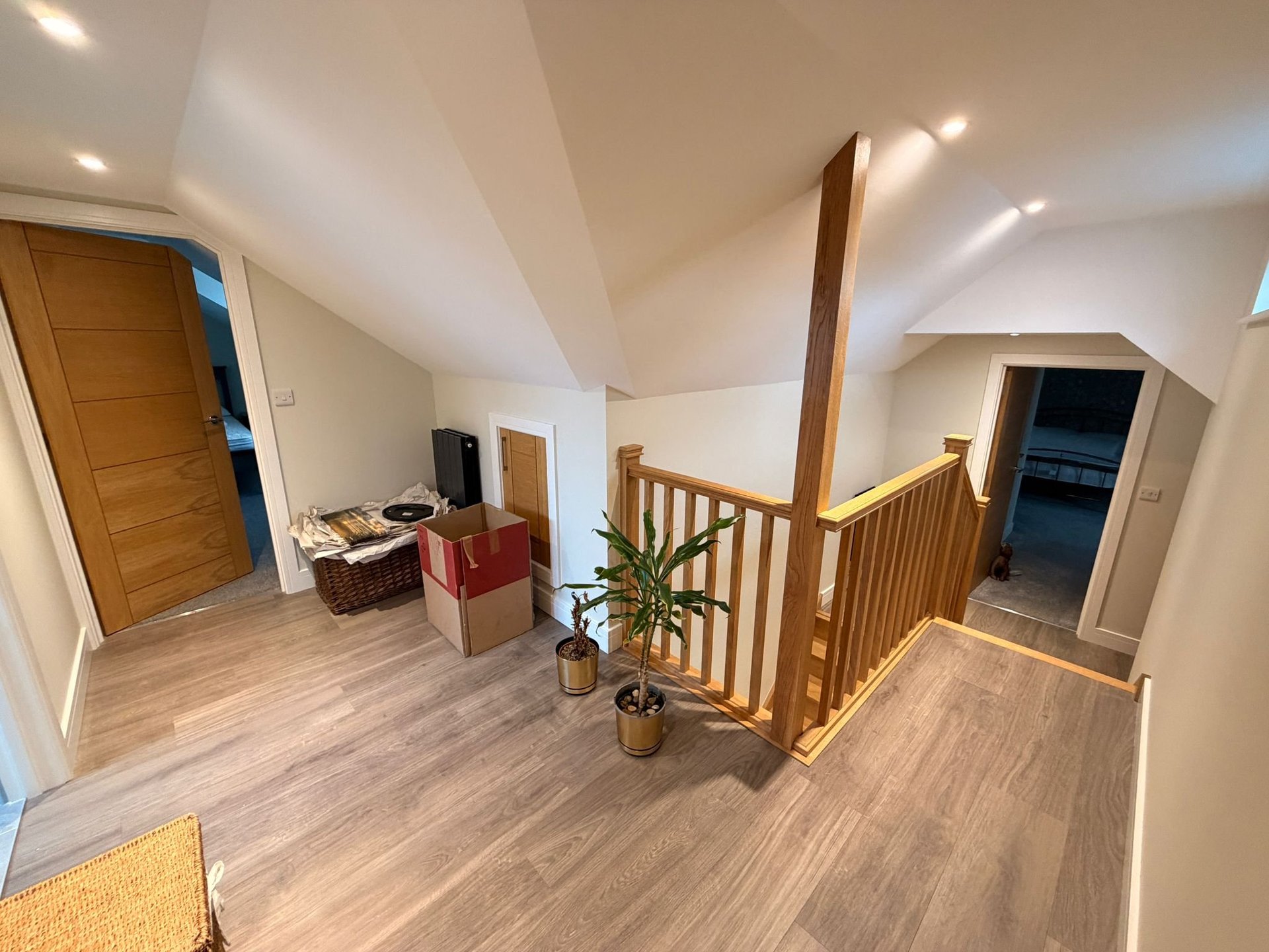 Bright attic loft space with wooden flooring, vaulted ceiling with skylight, wooden railing, and multiple doorways leading to different rooms.