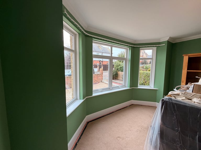 Empty room with green walls, bay windows overlooking a garden, and beige carpeting during renovation